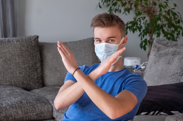 Guy dans un masque médical avec les bras croisés, montrant l'arrêt du coronavirus. L'homme se tient la main devant le visage