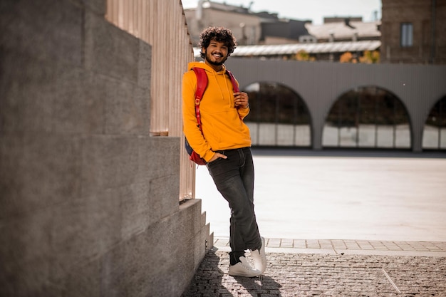 Guy dans un sweat à capuche. Jeune homme aux cheveux noirs en sweat à capuche orange avec un sac à dos