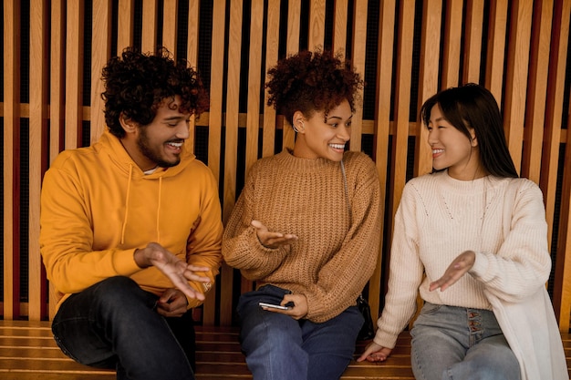 Guy et deux filles assis sur un banc avec smartphone