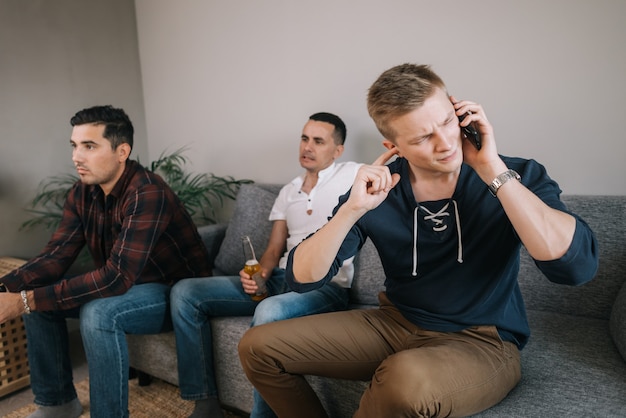 Guy essayant de parler au téléphone derrière l'homme, ses amis regardent la télévision