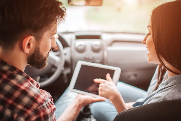 Guy est assis dans la voiture avec une fille et regarde la tablette avec un écran sombre.