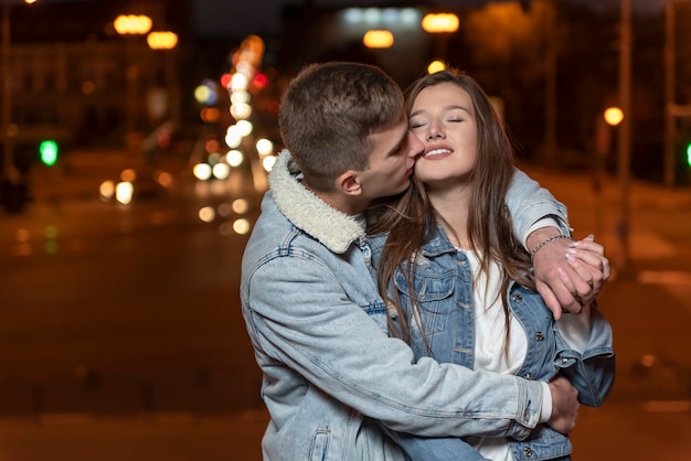 Guy étreint doucement et embrasse sa petite amie sur fond de ville en soirée Rendez-vous romantique