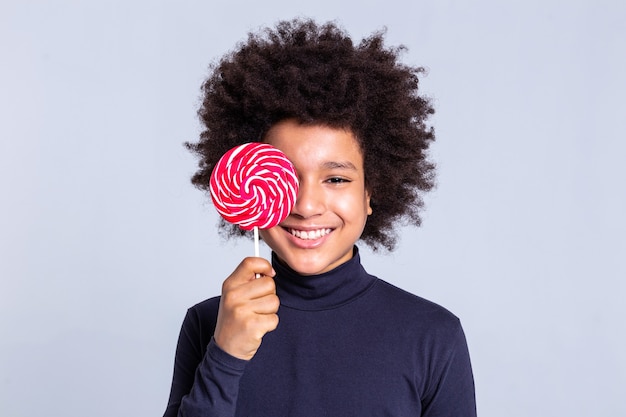 Photo guy fermant le visage. enfant gai avec des cheveux sauvages couvrant le visage avec de gros bonbons et montrant son large sourire