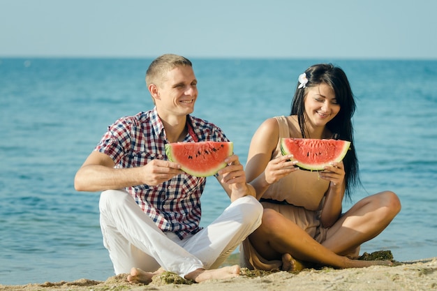 Guy et une fille au bord de la mer mangeant une pastèque rouge mûre