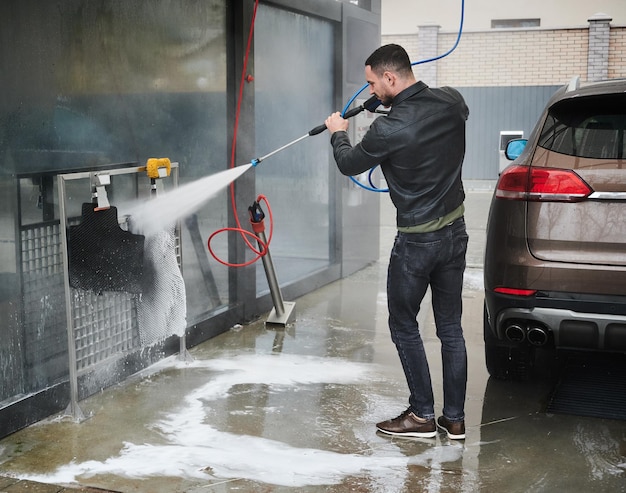 Guy laver les tapis de voiture au lavage automatique avec un pistolet à eau