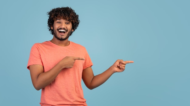 Guy oriental excité pointant vers l'espace de copie sur bleu