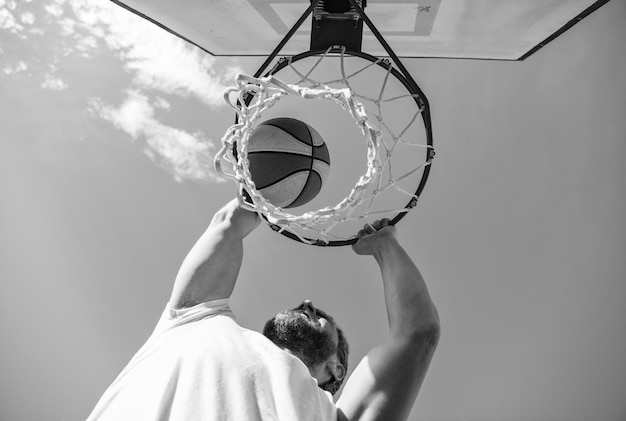 Guy plongeant un ballon de basket dans un anneau net avec les mains gagnantes