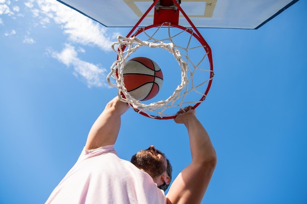 Guy plongeant un ballon de basket dans un anneau net avec les mains gagnantes