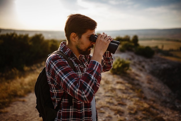 Guy regardant des jumelles dans l'homme de la colline en t-shirt avec sac à dos