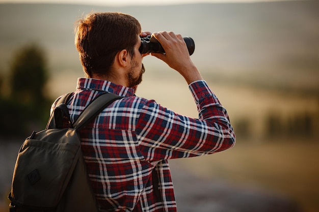 Guy regardant des jumelles dans l'homme de la colline en t-shirt avec sac à dos