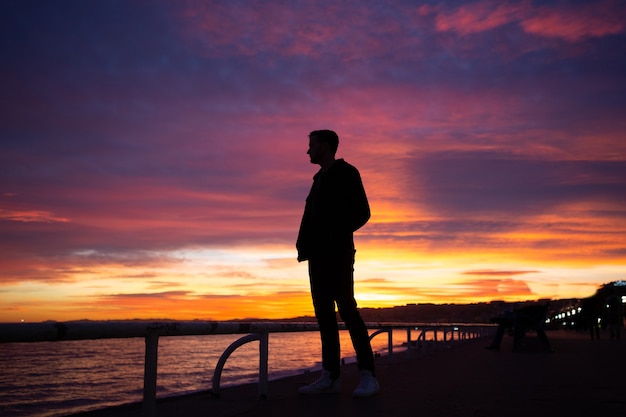Guy regardant magnifique coucher de soleil sur la rive de la mer à Nice, France.