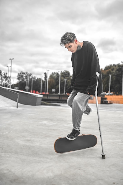 Guy s'appuyant sur des béquilles et touchant la planche à roulettes avec le pied