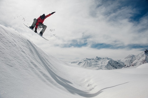 Guy saute sur une planche à neige contre un ciel bleu et des sommets enneigés