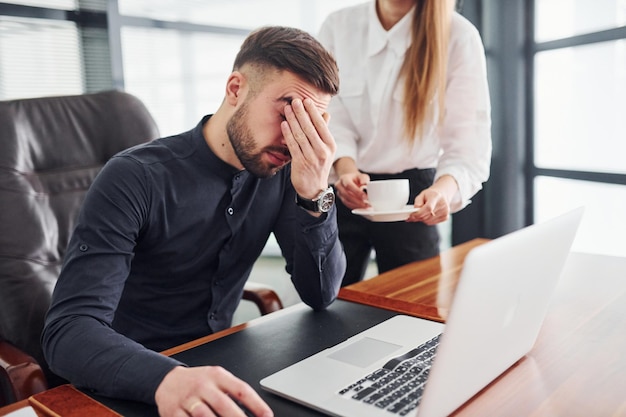 Guy se sent mal. Femme et homme en vêtements formels travaillant ensemble à l'intérieur au bureau par table.