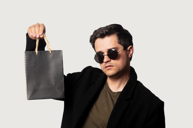 Guy de style en manteau noir et lunettes de soleil avec petit sac à provisions