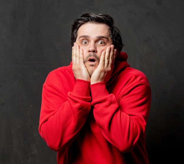 Guy surpris blanc en sweat-shirt rouge sur un mur sombre