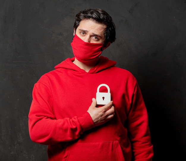 Guy en sweat-shirt rouge et masque facial maintenez le verrou sur le mur sombre