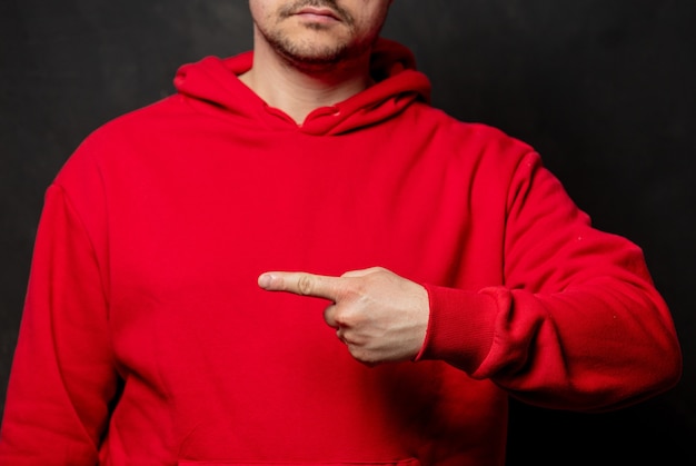 Guy en sweat-shirt rouge montre le geste du doigt sur le mur sombre