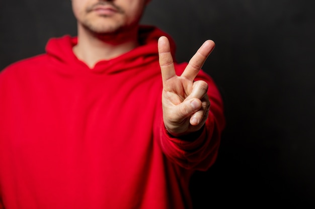 Guy en sweat-shirt rouge montre le geste OK sur un mur sombre