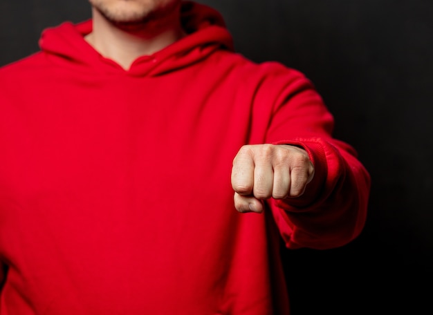 Guy en sweat-shirt rouge montrent le geste du poing sur un mur sombre