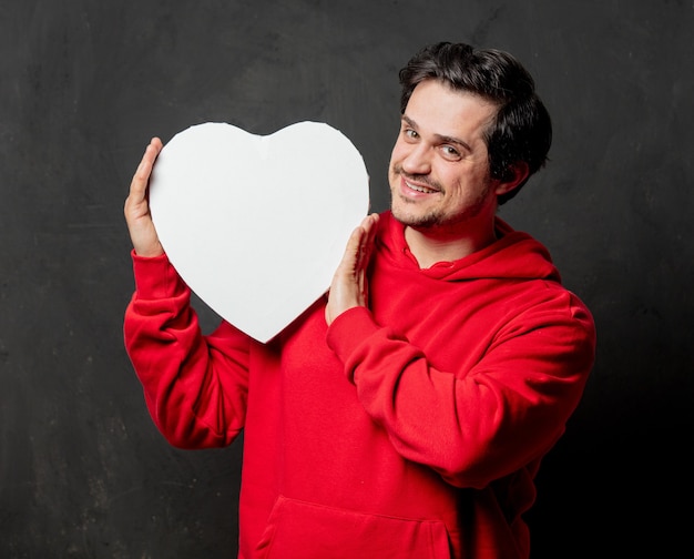 Guy en sweat-shirt rouge tenir cadre en forme de coeur sur un mur sombre