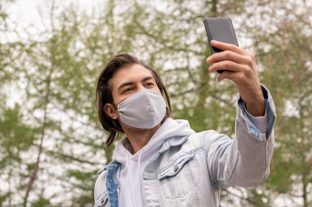 Guy en veste en jean et masque de protection tenant le smartphone devant son visage