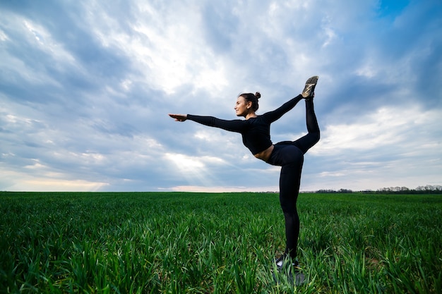 Gymnaste de belle fille sur l'herbe verte faire du yoga. Une belle jeune femme sur une pelouse verte exécute des éléments acrobatiques. gymnaste flexible en noir fait le poirier en split