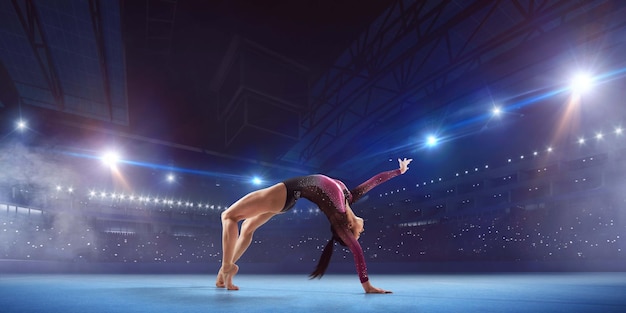 Gymnaste féminine faisant un tour compliqué sur la poutre d'équilibre de gymnastique dans une arène professionnelle