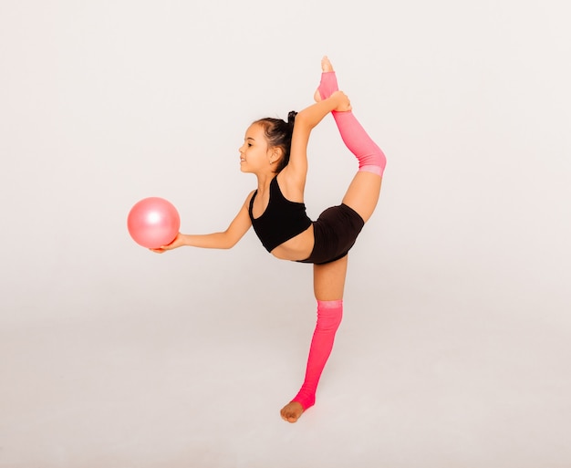 Gymnastique artistique. Petite fille flexible joue avec une balle sur fond blanc.