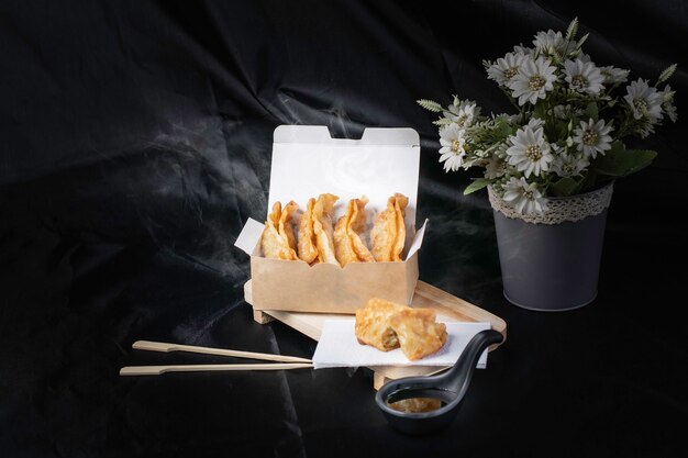 Gyoza frit, frites chaudes dans une boîte en carton fumé, fond noir.