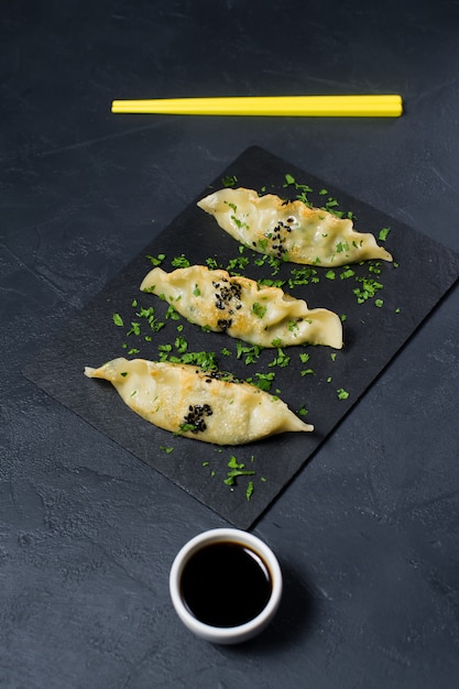 Gyoza japonais frit sur un plateau en pierre noire, baguettes jaunes.