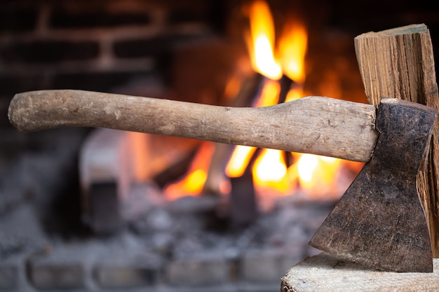 Une hache coincée dans une souche en bois près d'une cheminée en feu. Le concept de confort et de détente au village.