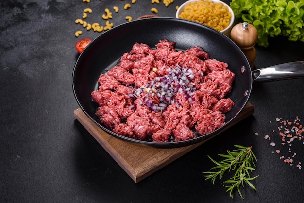 Hachis cru frais avec des épices et des herbes sur un fond de béton foncé