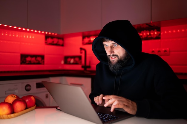 Un hacker dans un sweat à capuche noir est assis devant un ordinateur portable piratant le système de sécurité Internet