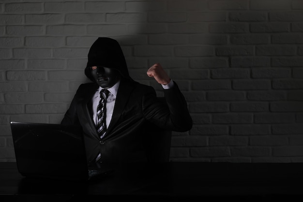 Hacker en masque noir et capuche à la table devant le moniteur