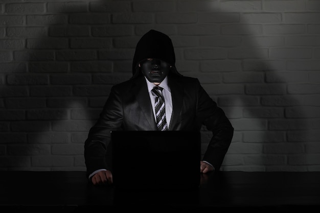 Hacker en masque noir et capuche à la table devant le moniteur