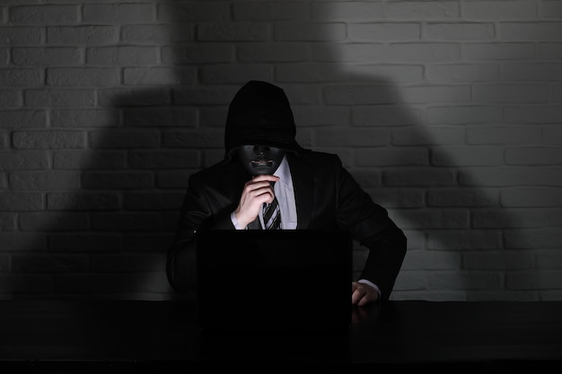 Hacker en masque noir et capuche à la table devant le moniteur