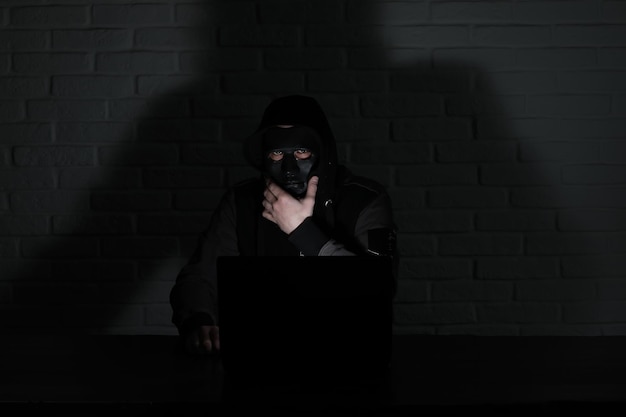 Hacker en masque noir et capuche à la table devant le moniteur