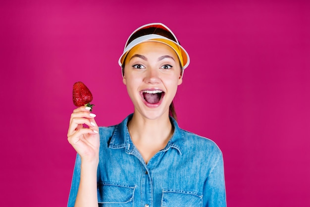 Haha dit la fille dans la visière tenant une fraise dans ses mains fond rose