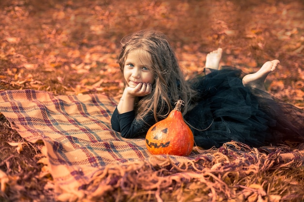 Halloween une jolie fille aux cheveux longs se trouve sur une couverture orange dans le parc à côté d'une drôle de citrouille