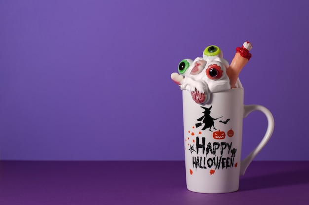 Halloween monstre secouer dans une grande tasse sur fond violet avec espace de copie. Crème fouettée avec des bonbons pour les yeux, les doigts, le cerveau et le crâne. Boisson effrayante.