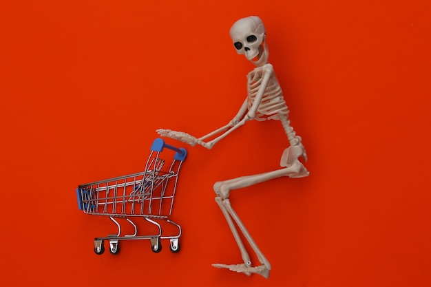 Halloween, thème effrayant. Squelette et caddie sur orange.