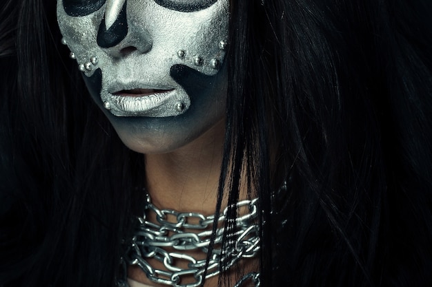 Halloween et thème de maquillage créatif: modèle de belle fille avec un corps noir avec peinture de crâne de masque argenté sur un mur sombre