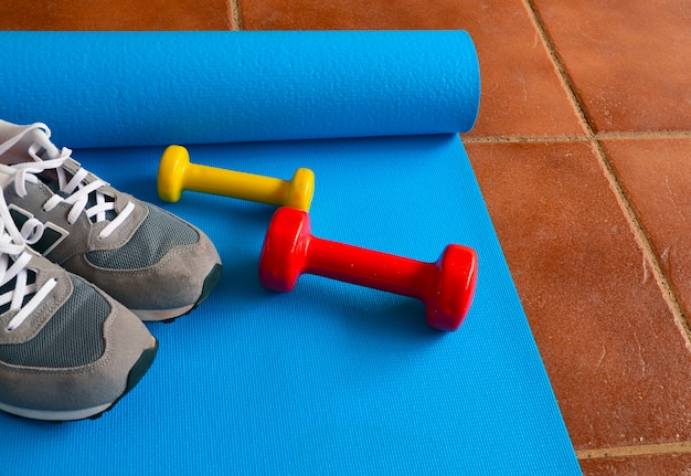 Haltères colorés, baskets et tapis de yoga bleus