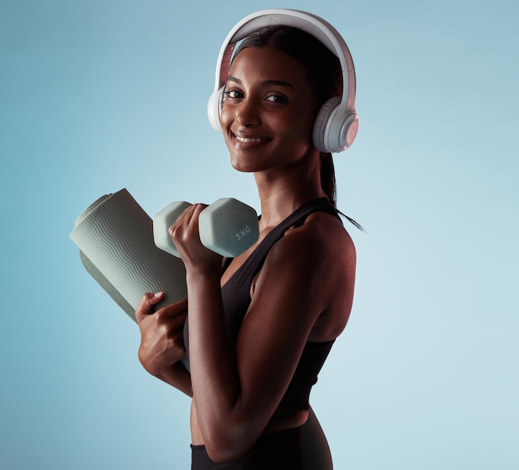 Photo haltères de femme et écouteurs de musique pour l'entraînement en studio sur fond bleu pour l'exercice d'entraînement de tapis de yoga ou de pilates portrait sourire ou modèle de fitness heureux avec radio de poids ou podcast de santé