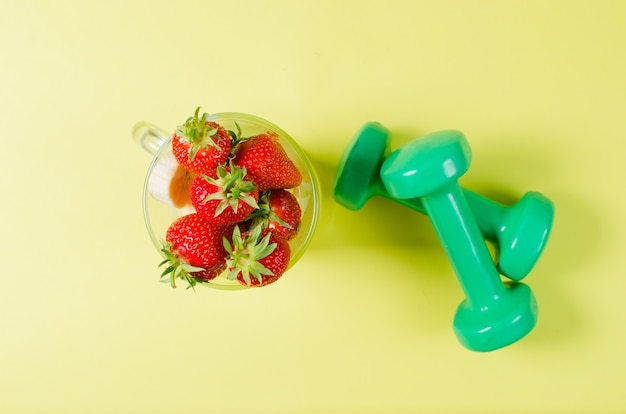 Haltères de fraise et de sport reposent sur une surface jaune clair