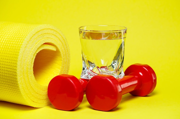 Haltères rouges, un verre d'eau, un tapis jaune, fond coloré, sports, boisson énergisante, équipement pour la salle de gym