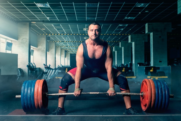 L'haltérophile masculin se prépare à tirer des haltères lourdes, soulevé de terre, intérieur de la salle de sport. Entraînement d'haltérophilie dans un club de sport ou de fitness, musculation