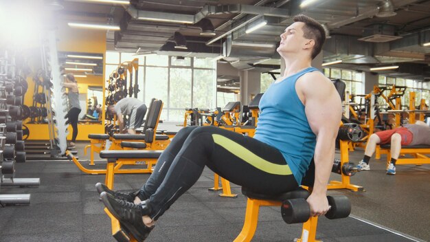 Haltérophilie dans la salle de sport - un athlète musclé s'entraîne pour les biceps avec des haltères, gros plan