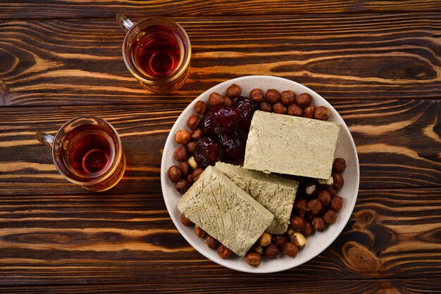 Halva savoureux avec du thé, des noix, des fruits secs sur une table en bois